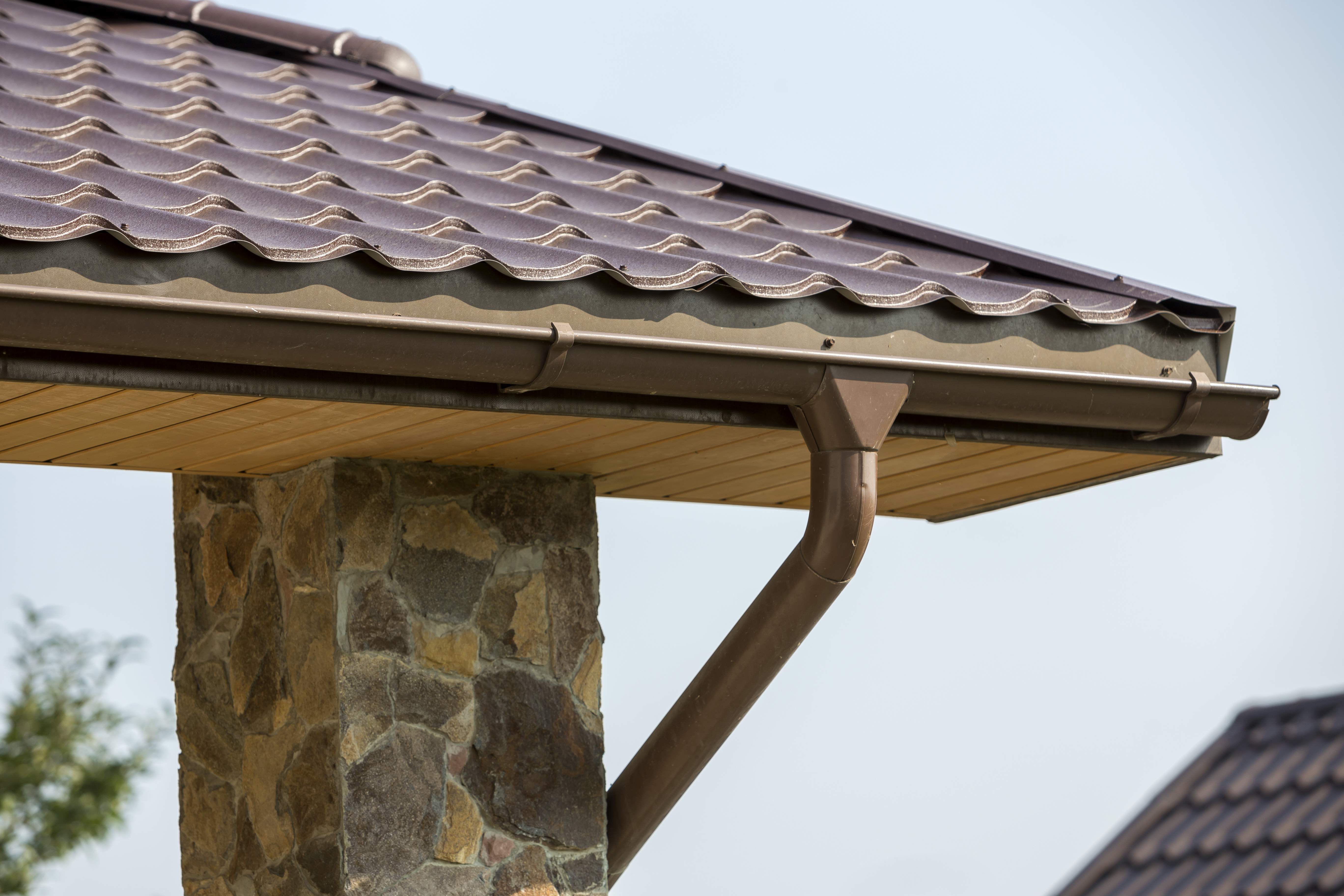 Installed aluminum gutter system with downspout on stone pillar home