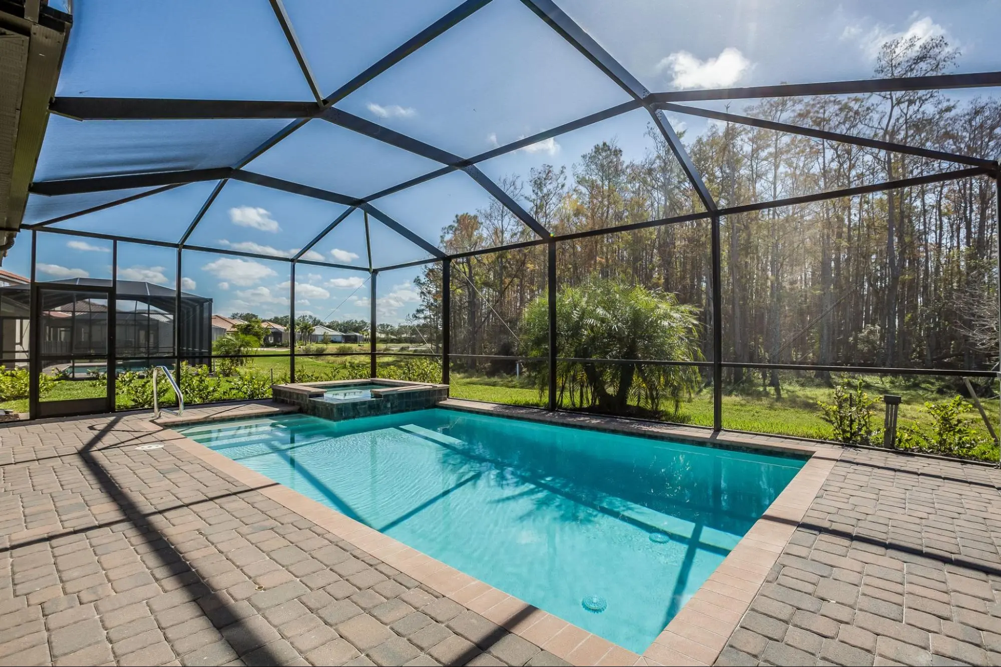 Aluminum screen enclosure over a backyard pool and spa with paver deck