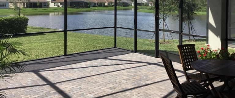 Paver patio under a lanai beside a lake